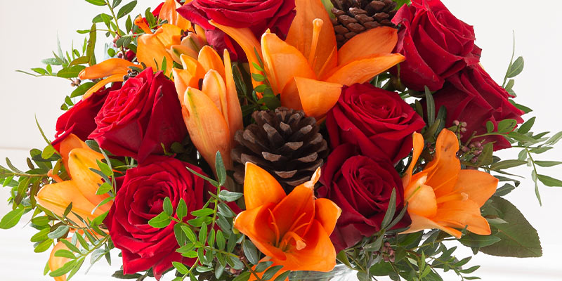 Christmas bouquet of red roses, orange lilies, and pinecones. 